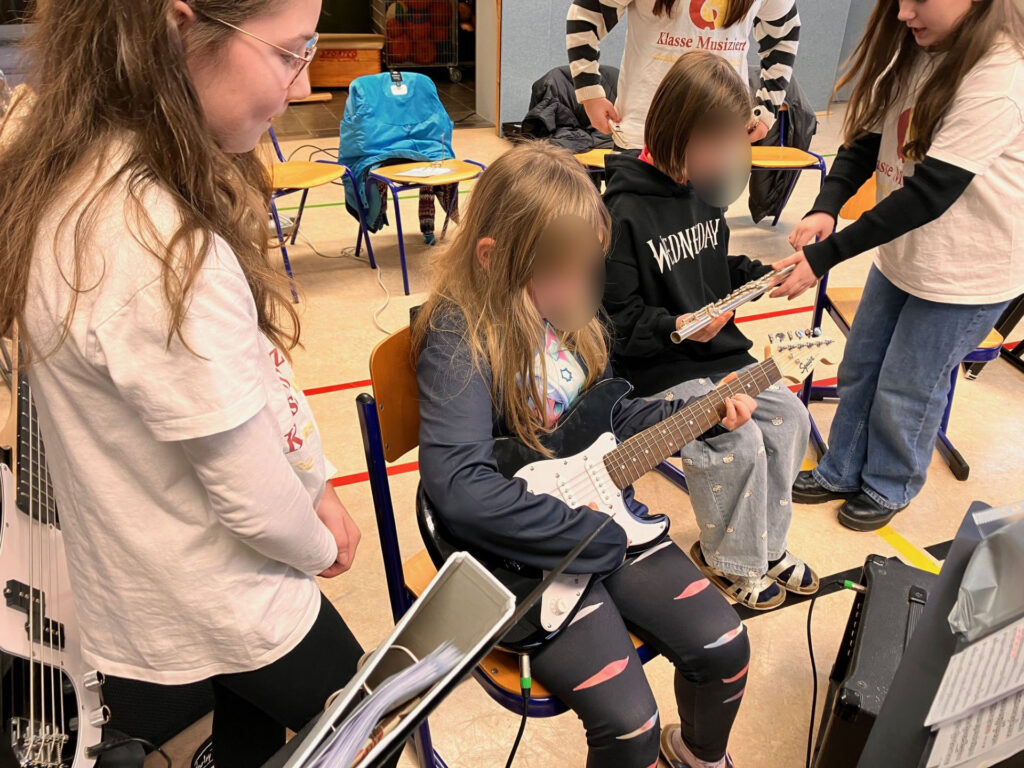 Schülerinnen üben an Gitarren in einem Klassenraum.