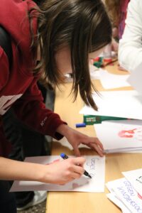 Schülerin schreibt mit einem Stift auf ein Blatt Papier an einem Tisch.