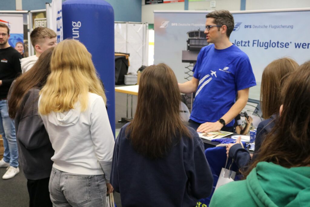Ein Mann erklärt Schülern an einem Messestand etwas über Fluglotsen.