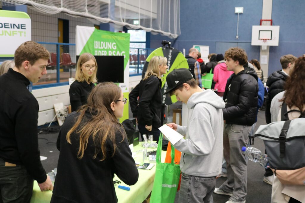 Schüler und SchülerInnen an Ständen einer Ausbildungsmesse in einer Sporthalle.