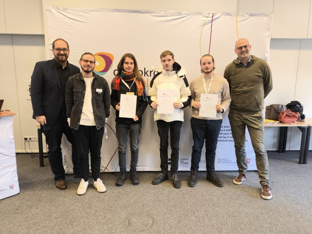Gruppenfoto von fünf Personen mit Zertifikaten vor einem Banner.