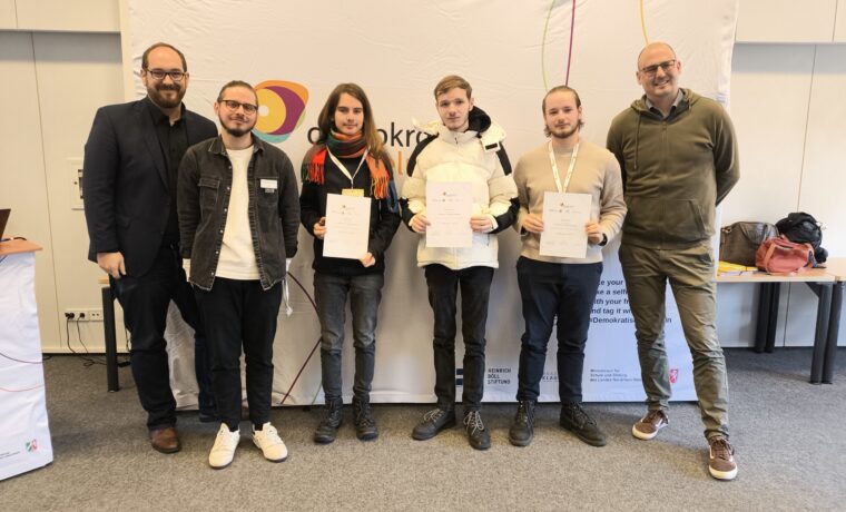 Gruppenfoto von fünf Personen mit Zertifikaten vor einem Banner.
