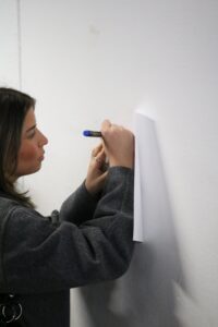 Eine Person schreibt mit einem Stift auf ein Blatt Papier, das an einer Wand befestigt ist.