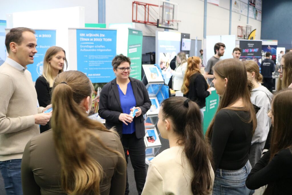 Messe mit mehreren Personen, die an Ständen Informationen austauschen.