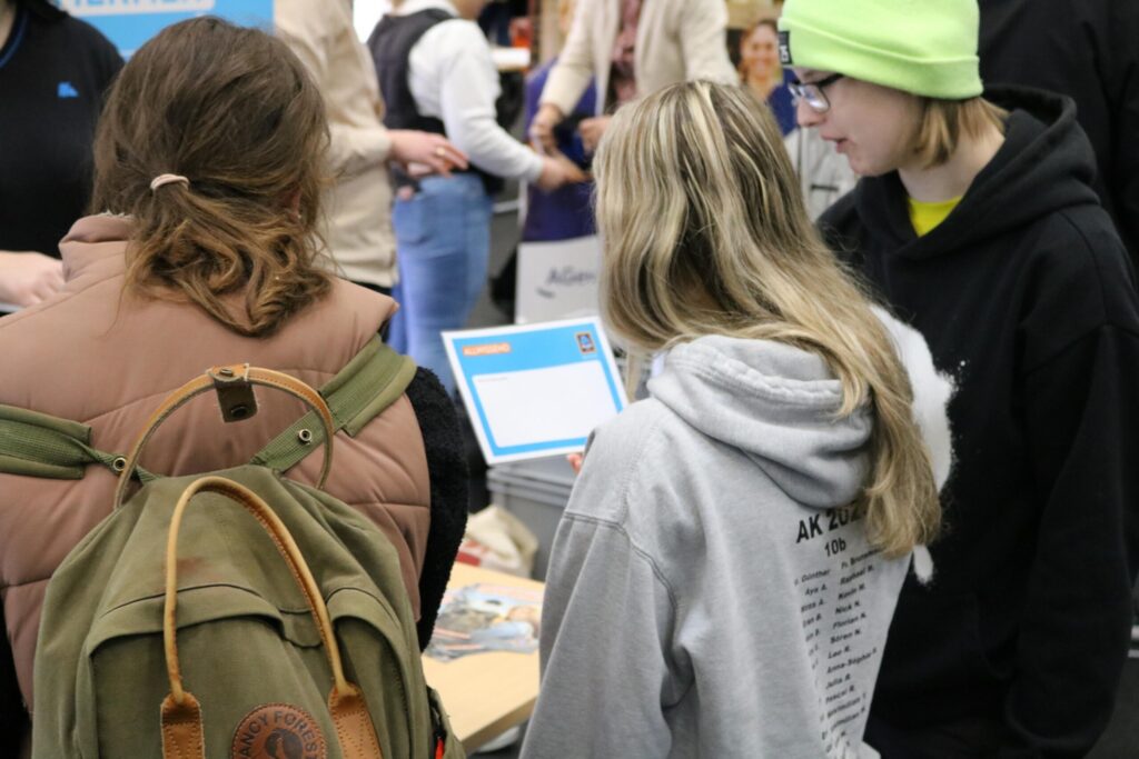 Drei Schülerinnen betrachten Informationsmaterial an einem Stand.
