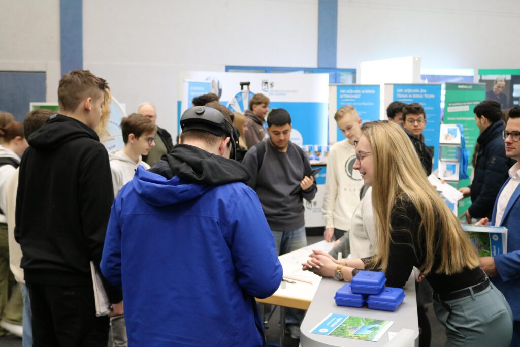 Messe mit mehreren Personen, die an Ständen Informationen austauschen.
