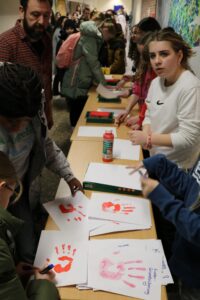 Schülerinnen und Schüler gestalten Handabdrücke auf Papier an einem Tisch.