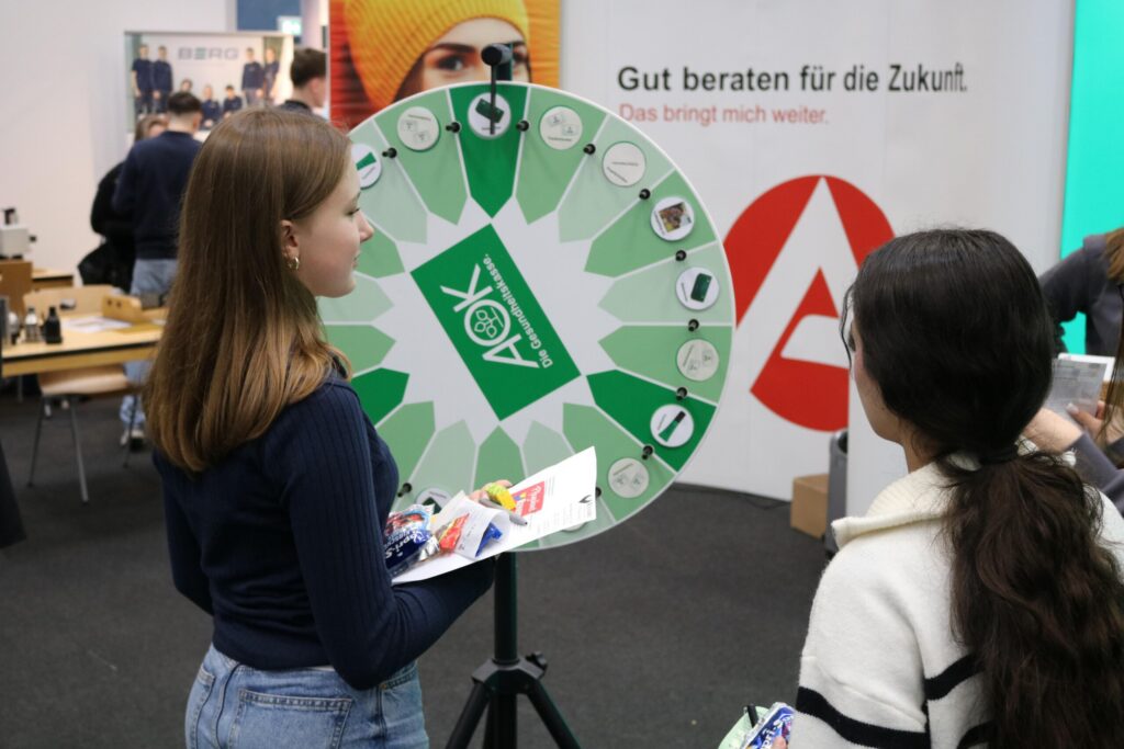Zwei Mädchen stehen vor einem Glücksrad mit verschiedenen Symbolen.