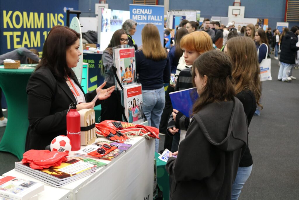 Messe mit mehreren Ständen und Schülern, die Informationen sammeln.