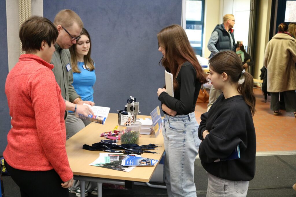Messestand mit Personen, die Informationen und Materialien ausgeben.