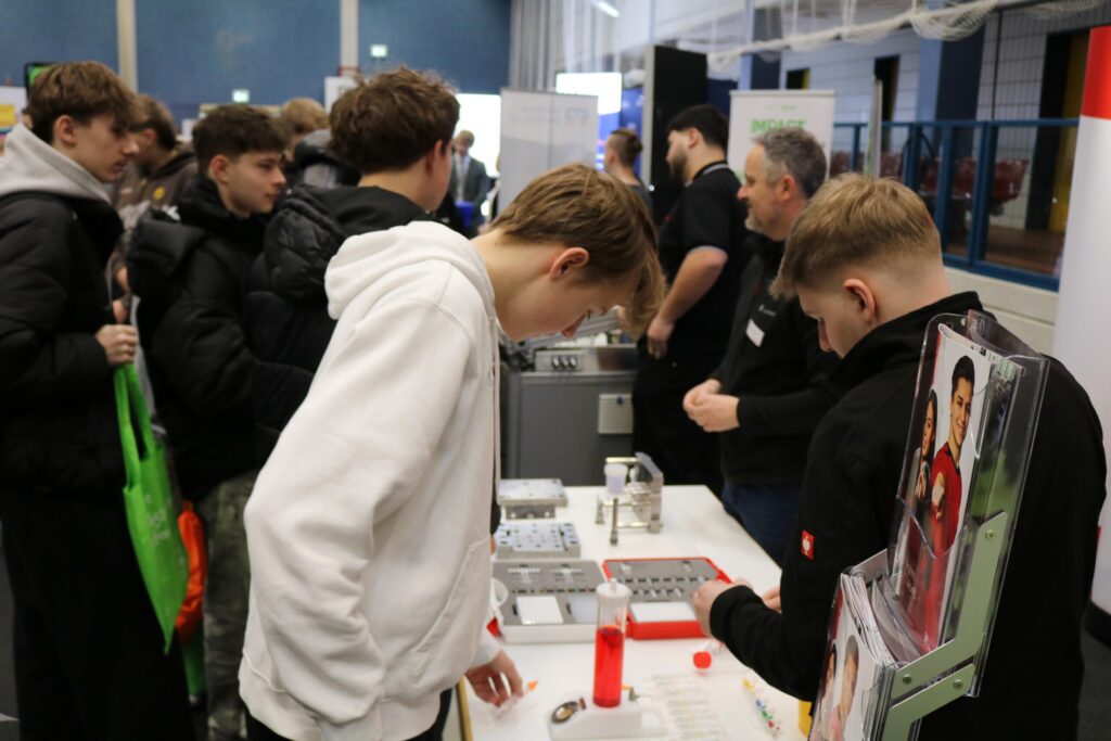 Schülerinnen und Schüler erkunden einen Messestand mit Präsentationen und Produkten.