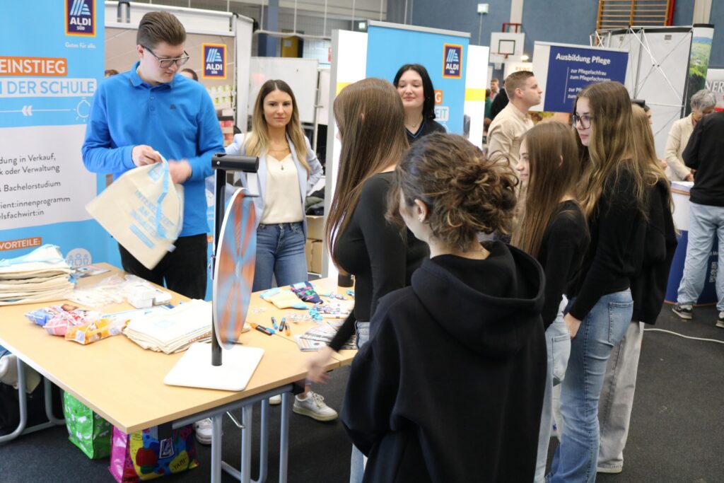 Schülerinnen und Schüler an einem Informationsstand in einer Sporthalle.