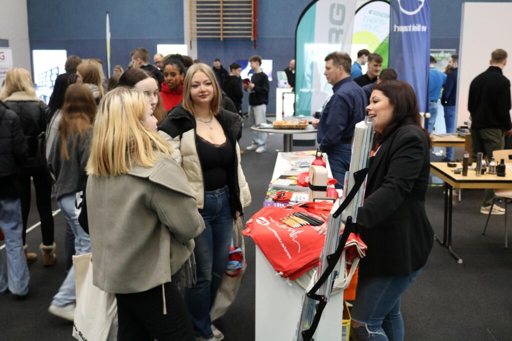 Besucherinnen sprechen mit einem Standpersonal auf einer Messe.