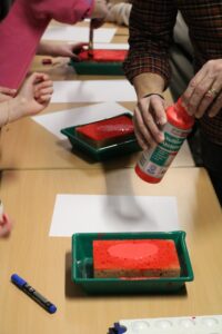 Schüler färben Schwämme mit roter Farbe auf einem Tisch.