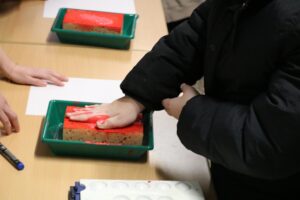 Ein Kind, das eine rote Fläche auf einen Schwamm drückt.