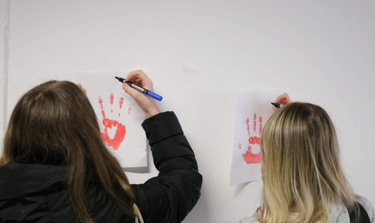 Zwei Schüler zeichnen mit Stiften auf Bilder von Handabdrücken.