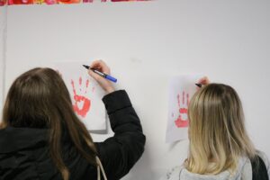 Zwei Schüler zeichnen mit Stiften auf Bilder von Handabdrücken.