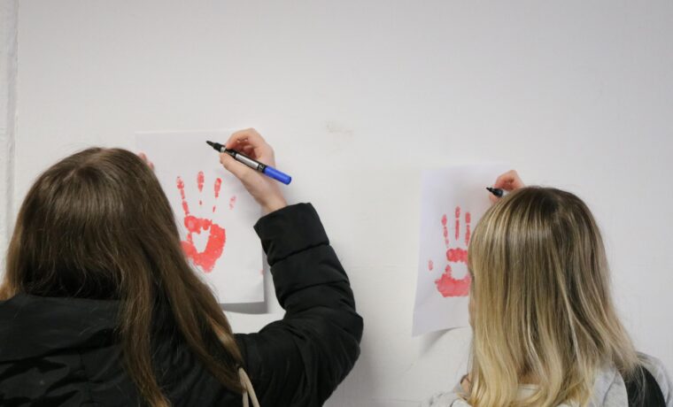 Zwei Schüler zeichnen mit Stiften auf Bilder von Handabdrücken.