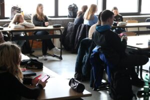 Schüler sitzen in einem Klassenzimmer, einige beschäftigen sich mit Handys.