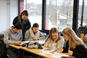 Schüler arbeiten an einem Tisch, während eine Lehrerin ihnen hilft.