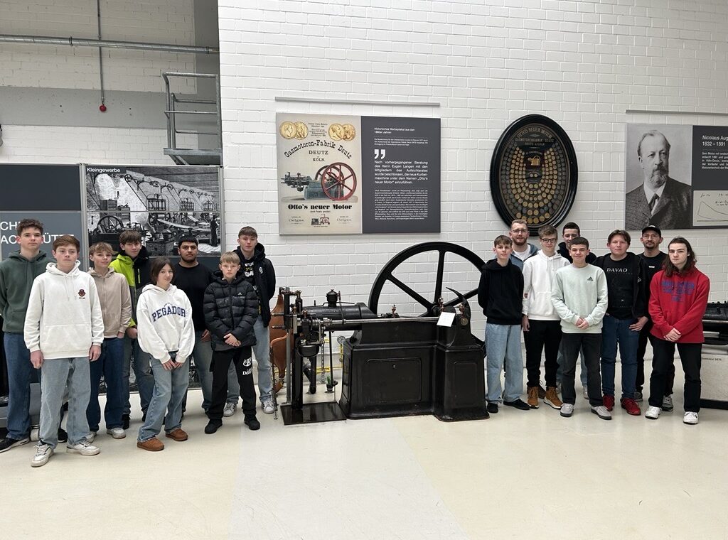 Gruppe von Schülern steht vor einer historischen Maschine in einem Technikmuseum.
