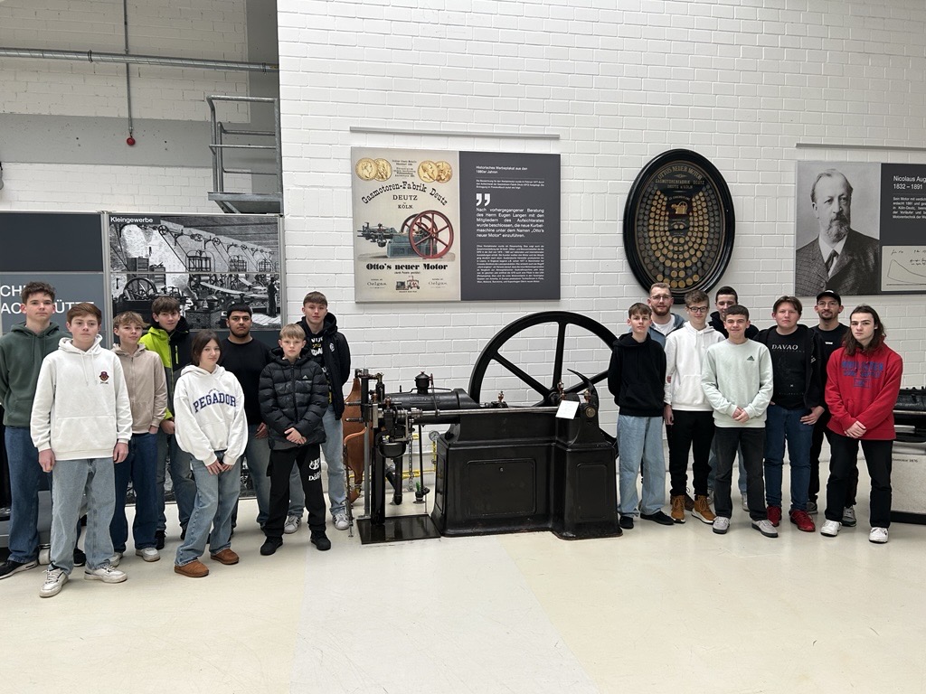 Gruppe von Schülern steht vor einer historischen Maschine in einem Technikmuseum.