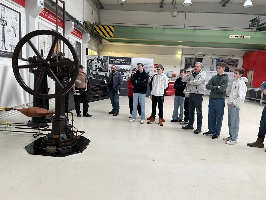 Besuchergruppe schaut sich eine historische Maschine in einem Museum an.