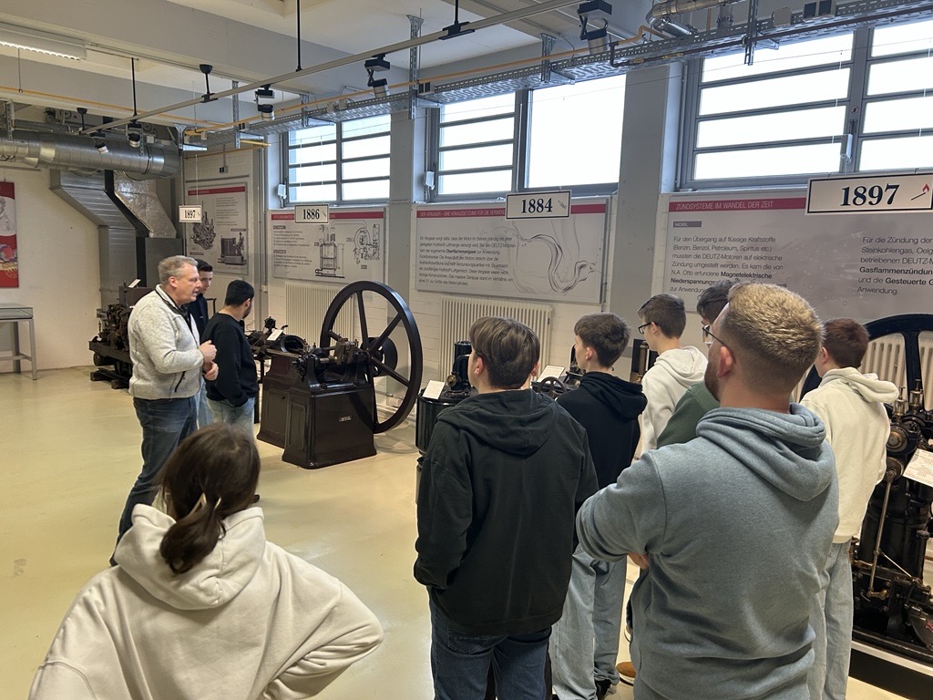 Gruppe von Schülern hört einem Lehrer zu, der Maschinen erklärt.
