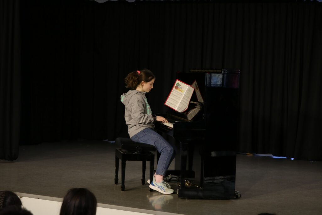 Ein Mädchen spielt Klavier auf einer Bühne mit schwarzem Vorhang.