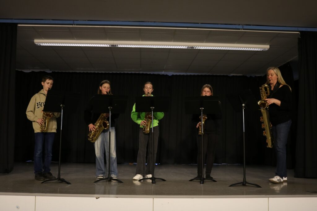 Fünf Personen mit Saxophonen auf einer Bühnenbühne.