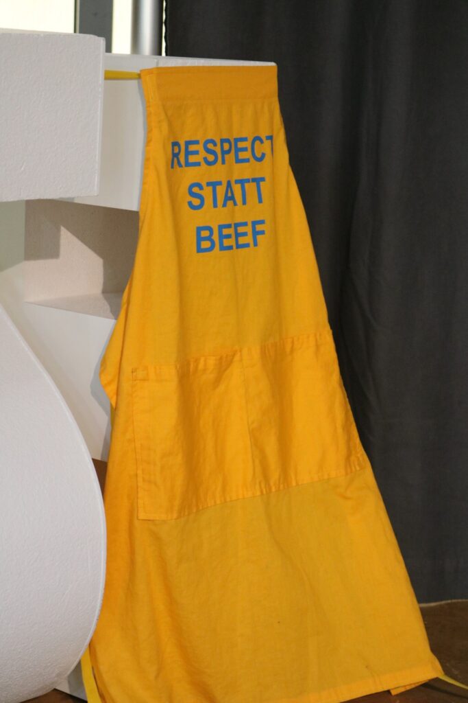 Gelbes T-Shirt mit der Aufschrift "RESPECT STATT BEEF" hängt an einer Kante.
