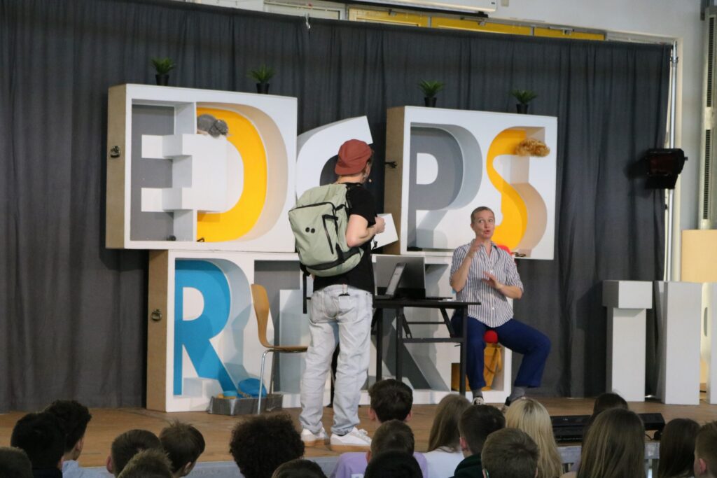 Ein Schüler mit Rucksack steht vor einem Redner auf einer Bühne.
