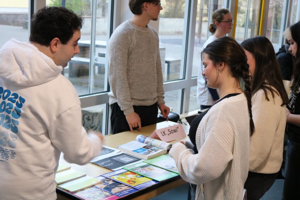 Schülerinnen und Schüler schauen sich Informationen am Tisch an.