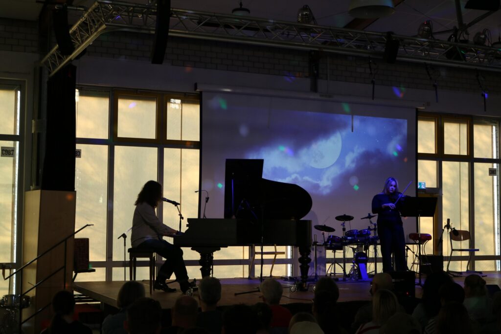 Schüler spielt Klavier auf einer Bühne, Hintergrund mit Musikvideo und Band.