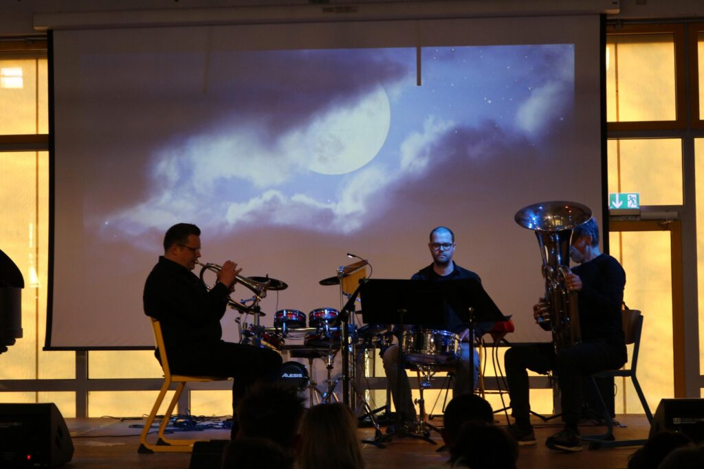 Musiker spielen auf der Bühne vor einem projizierten Mondbild.
