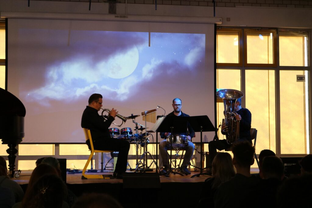 Drei Musiker spielen auf der Bühne vor einer Leinwand mit Mondmotiv.