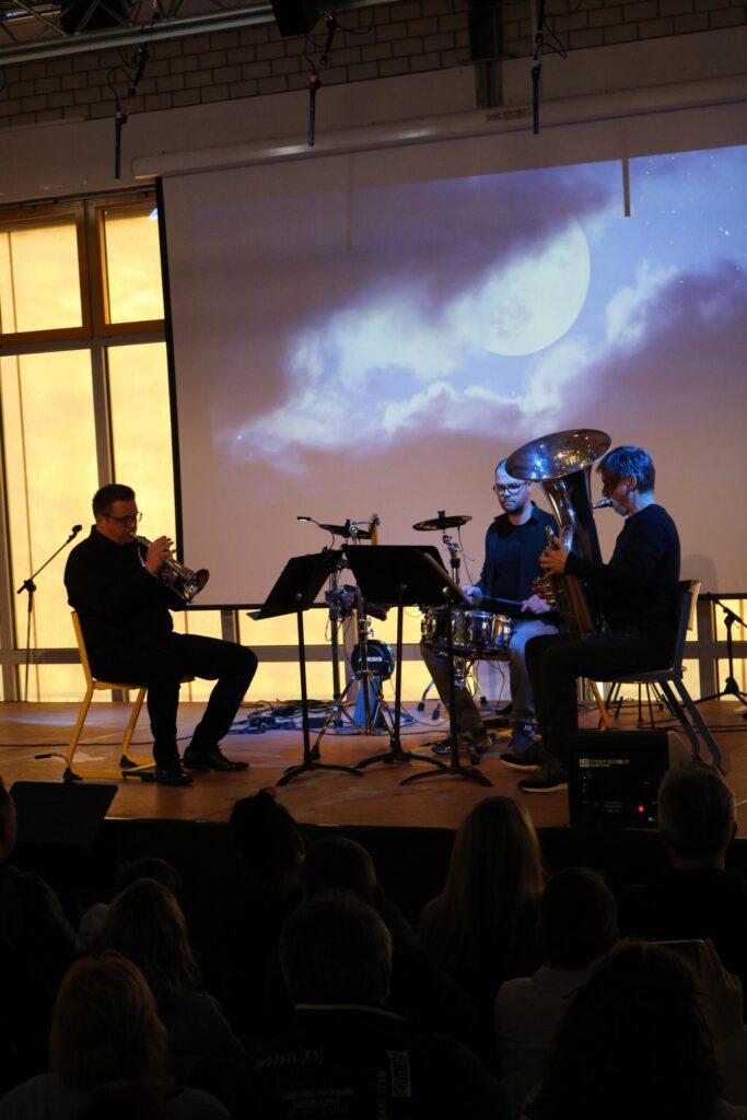 Musiker spielen auf der Bühne vor einer Projektion mit Wolken. Zuschauer im Vordergrund.