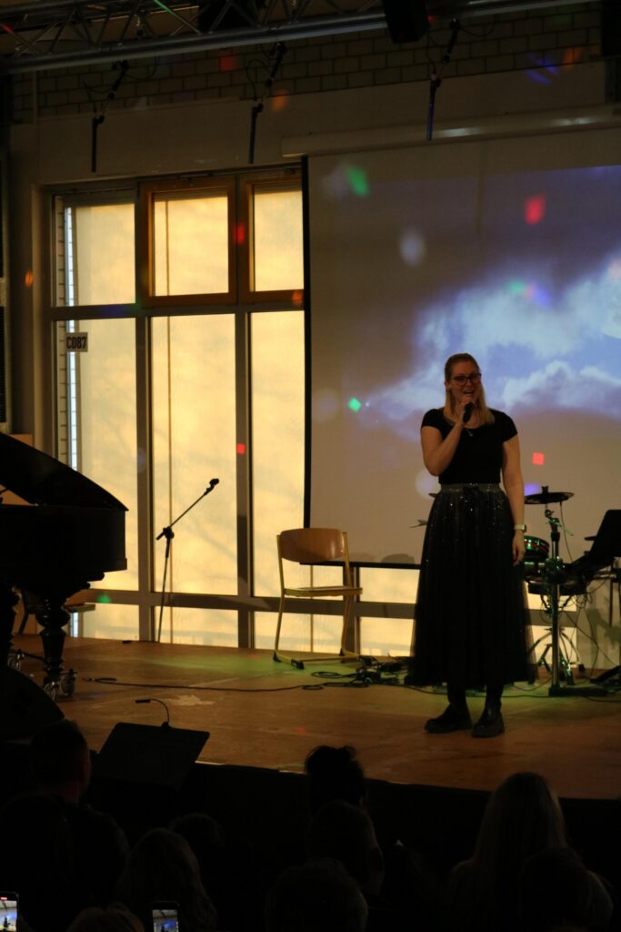 Eine Sängerin steht auf der Bühne vor einem Klavier und einem Band-Setup.