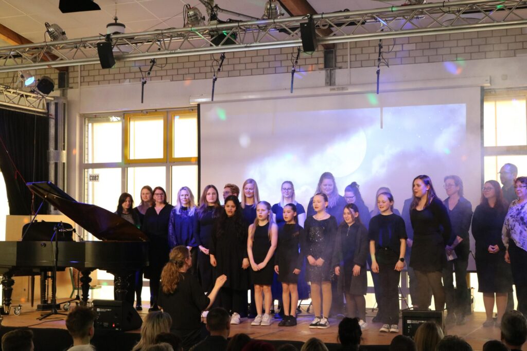 Choraufführung auf der Bühne mit Pianist und Publikum im Vordergrund.