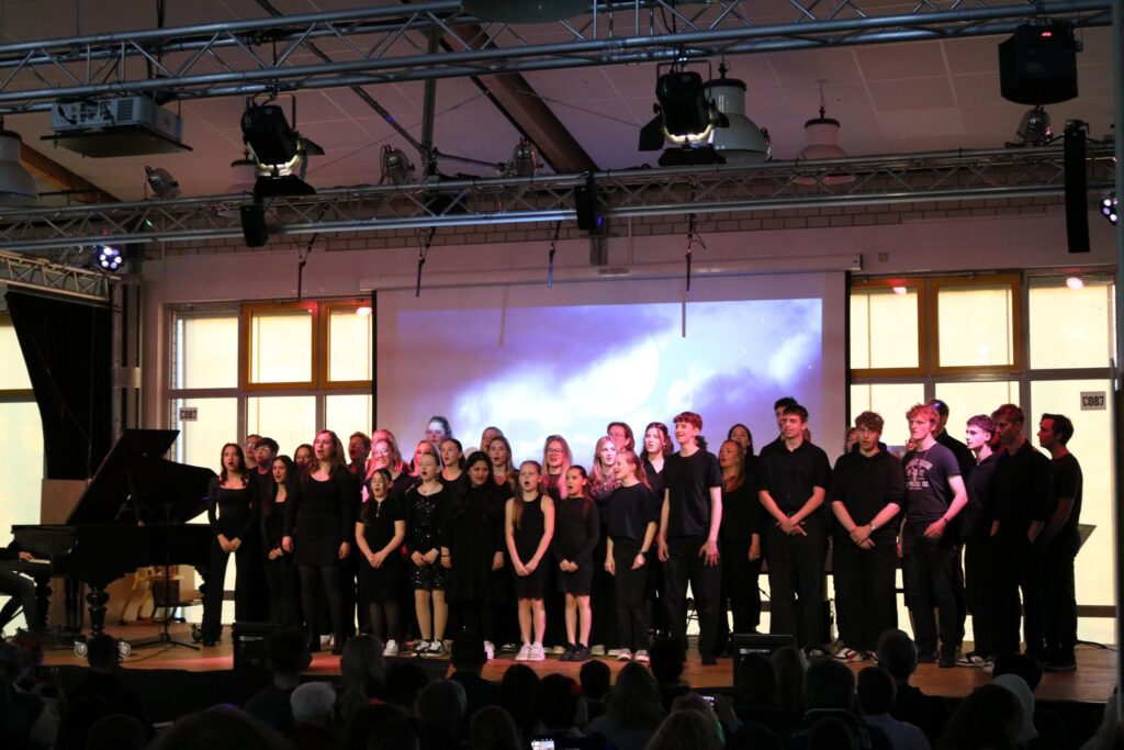 Schüler stehen auf der Bühne und singen, im Hintergrund ein Klavier.