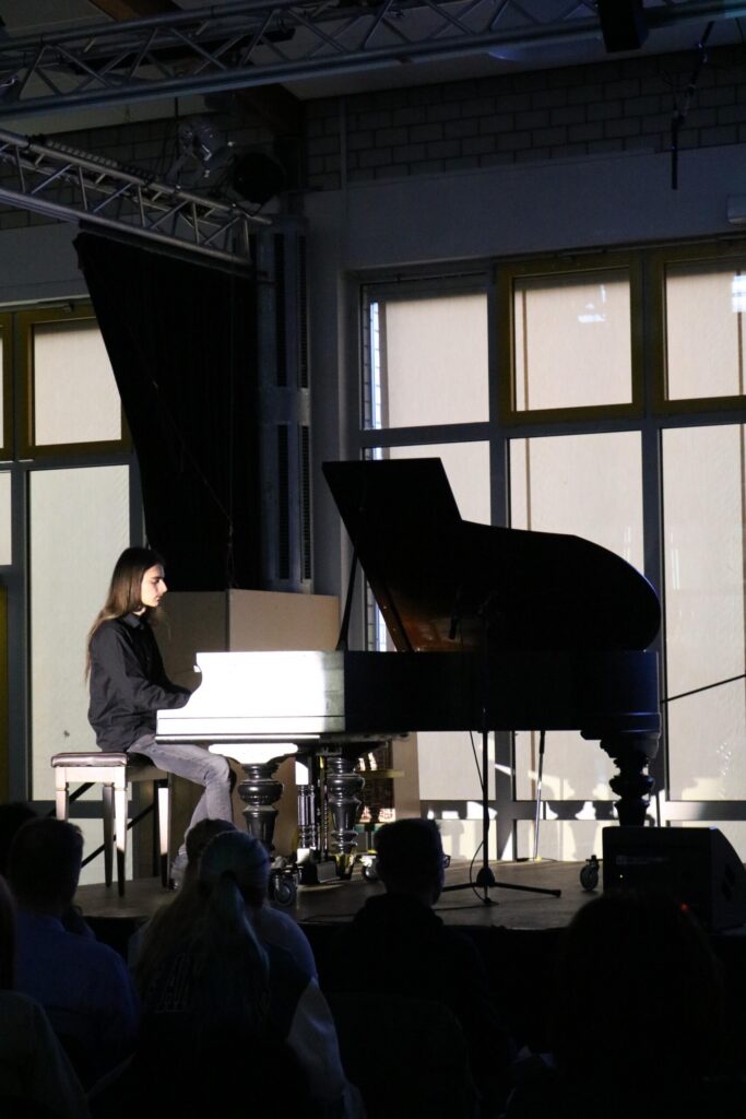 Schüler spielt Klavier auf einer Bühne vor Publikum.