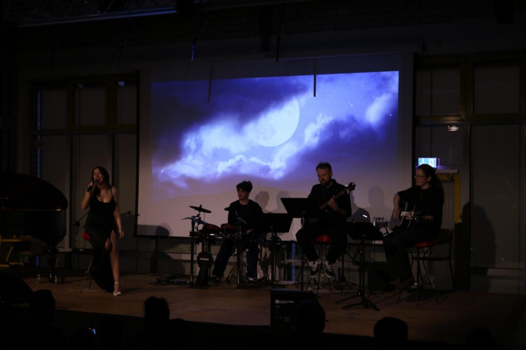 Musiker und Sängerin auf der Bühne vor einer projizierten Wolkenlandschaft.