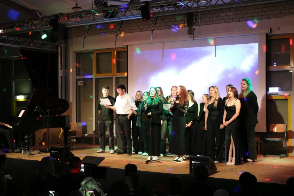 Schülerinnen und Schüler singen auf einer Bühne, im Hintergrund ein Klavier.