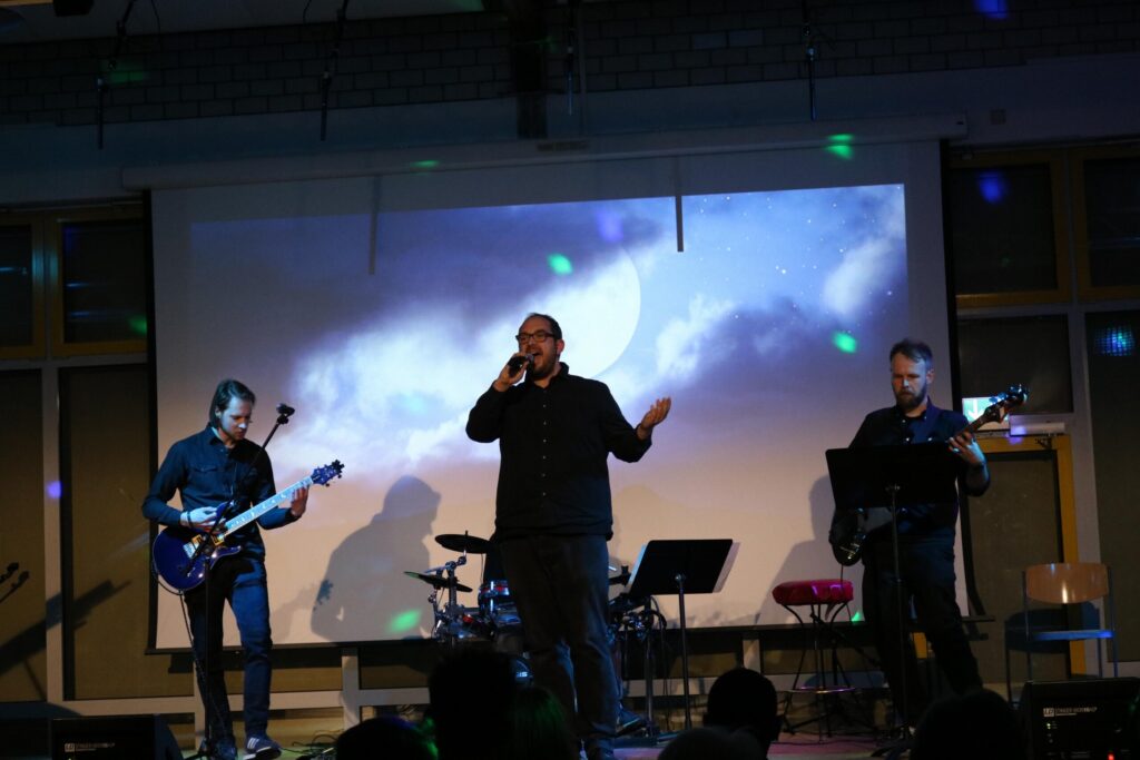 Musiker treten auf einer Bühne vor einer Leinwand mit Wolken und einem Mond auf.