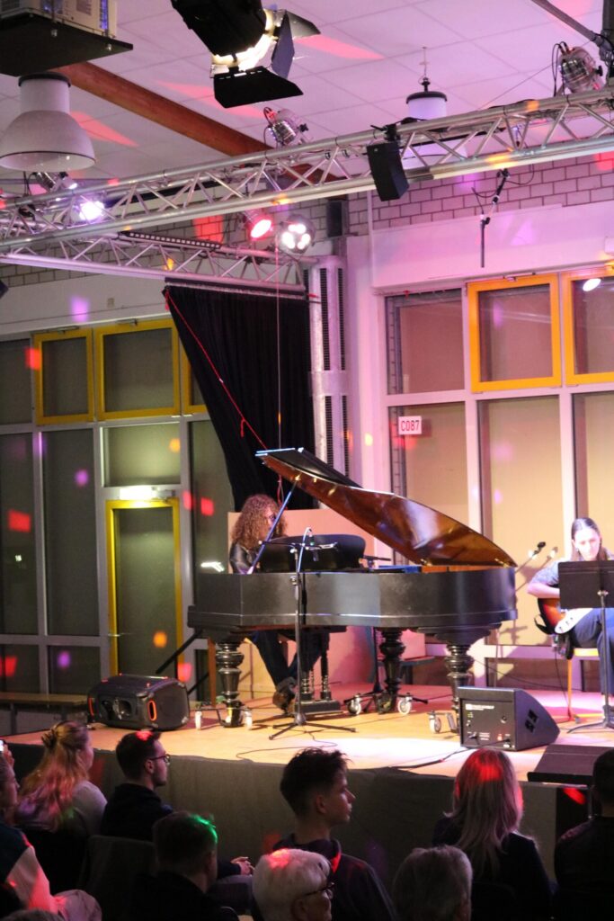 Ein Klavierkonzert mit Performern und Publikum in einem festlich beleuchteten Raum.