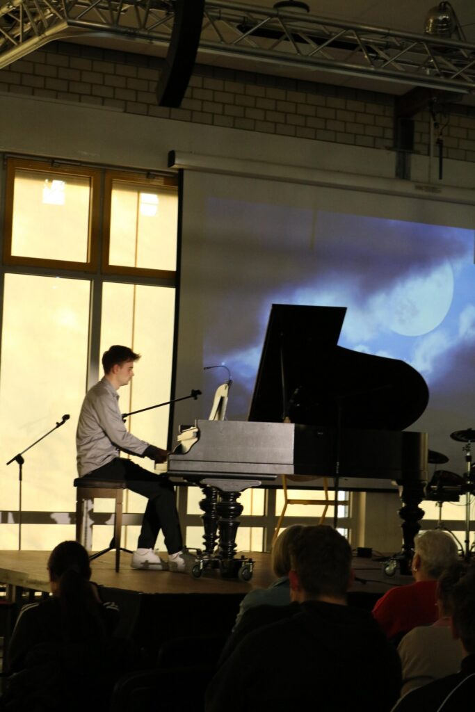 Junger Musiker spielt Klavier vor einer Leinwand mit visuellen Effekten.