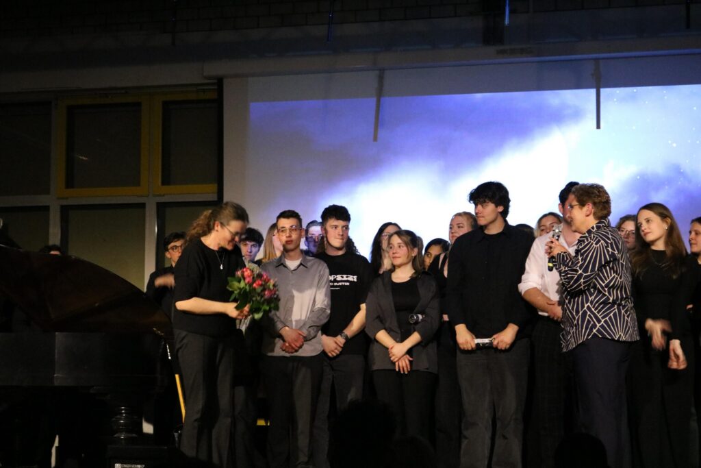 Schülerinnen und Schüler stehen auf der Bühne, eine Person erhält Blumen.