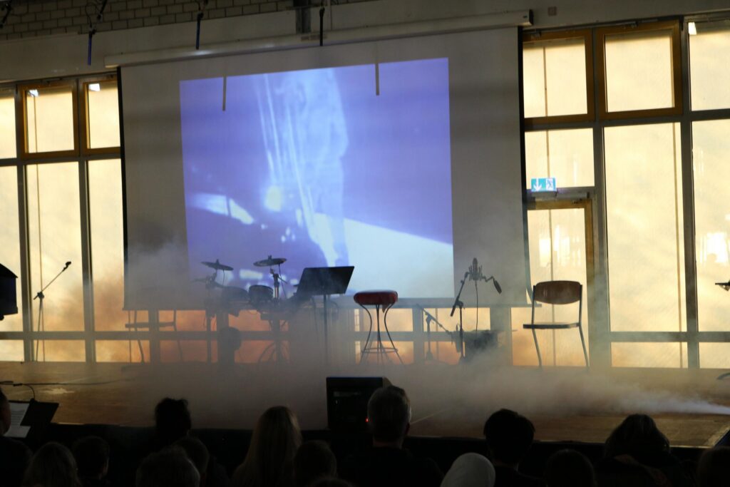 Bühne mit Nebel, Projektionsleinwand und Musikinstrumenten.