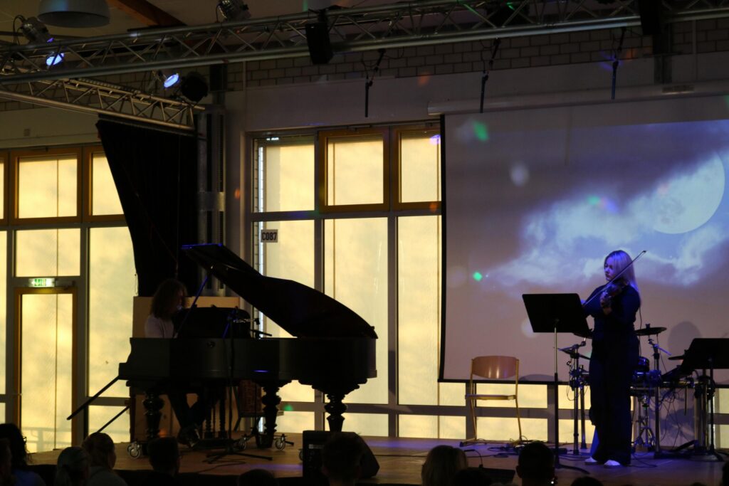 Die Bühne mit einem Klavier, einer Musikerin und einer Leinwand im Hintergrund.