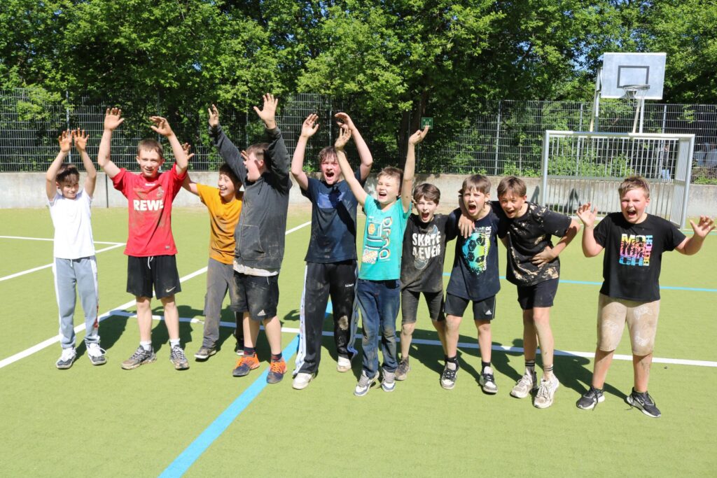 Gruppe von Kindern auf einem Sportplatz, die jubeln und lachen.